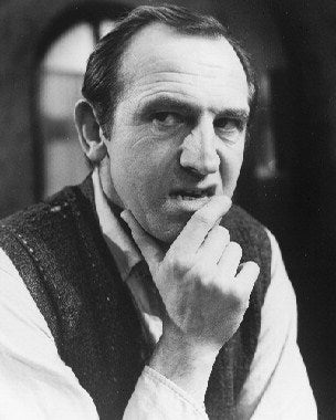 Leonard Rossiter in Rising Damp sitcom sitting on a sofa with humorous expression