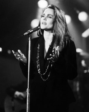 Belinda Carlisle performing live on stage with a vibrant background