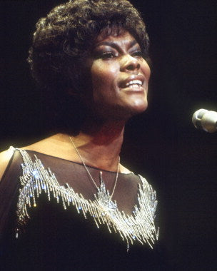Front view of Dionne Warwick fragrance bottle beside vinyl records from her greatest hits collection.