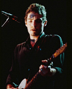 Jakob Dylan performing live on stage with guitar and microphone